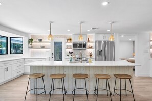 A modern kitchen with a large island, bar stools, and pendant lighting.