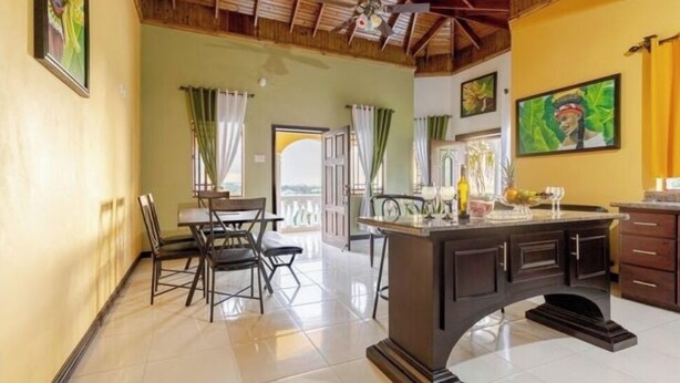 A dining area with a wooden ceiling, a central island with a glass top, and a view of the outdoors through a door.