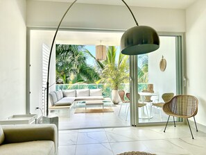 Una sala de estar moderna con un sofá, una mesa de centro y sillas, un ventanal con vista a palmeras y un ventanal corredizo que da a un área exterior.