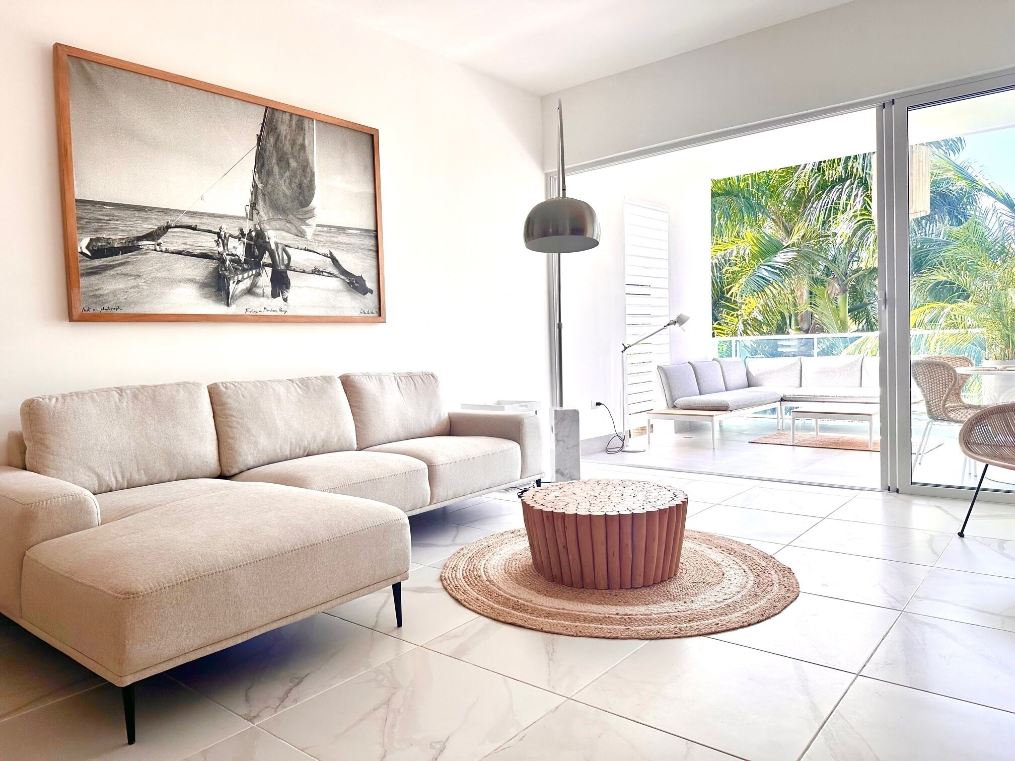 Un salon moderne avec un canapé d’angle beige, une table basse ronde et un grand tableau représentant un voilier accroché au mur.