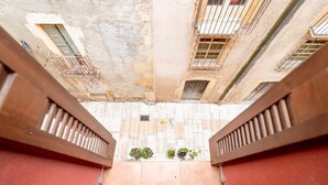 Vista de uma varanda, olhando para uma escadaria estreita com piso de azulejos e plantas em vasos.