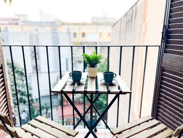 A balcony with a small table, two cups, and a potted plant.