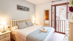 Quarto com cama, mesas de cabeceira, um criado-mudo, janela com vista e porta para outro cômodo.