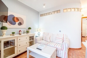 A living room with a striped sofa, a white coffee table, a cabinet with glass doors, and a wall-mounted abstract artwork.
