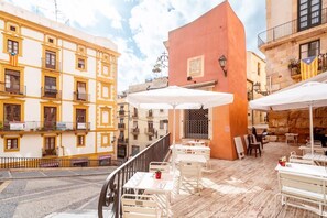 A terrace with outdoor seating, a red building, and yellow buildings in the background.