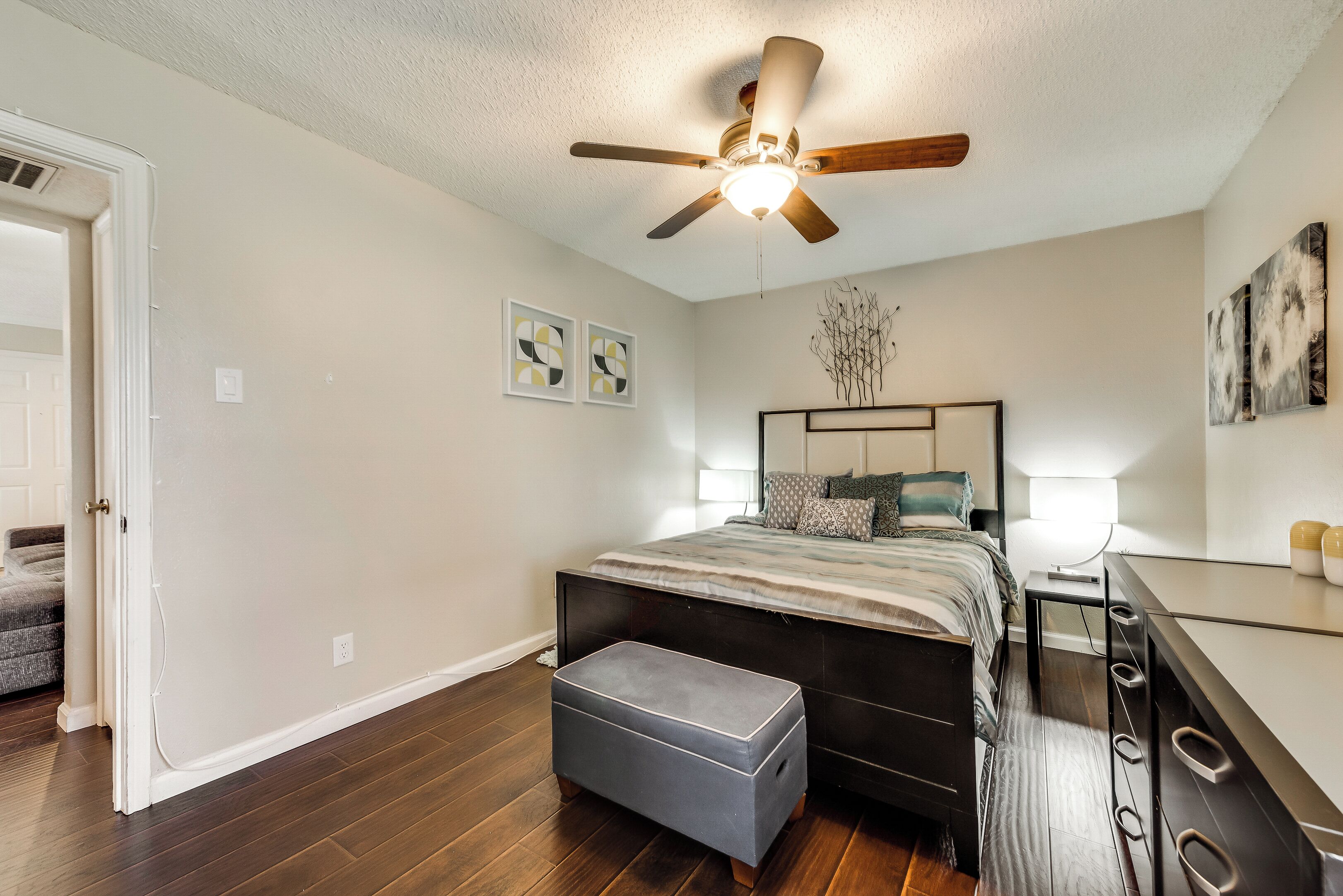 A bedroom with a bed, a ceiling fan, a nightstand, a dresser, and a small table.