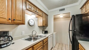 Eine Küche mit Holzausstattung, einem Edelstahlspülbecken, einer Kaffeemaschine, einem Toaster und einem Kühlschrank.