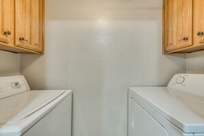 A laundry room with two white front-loading washing machines and wooden cabinets above them. - I24 - Apt|Patio|11mi to Convention Ctr|Sleeps 2 (Irving)