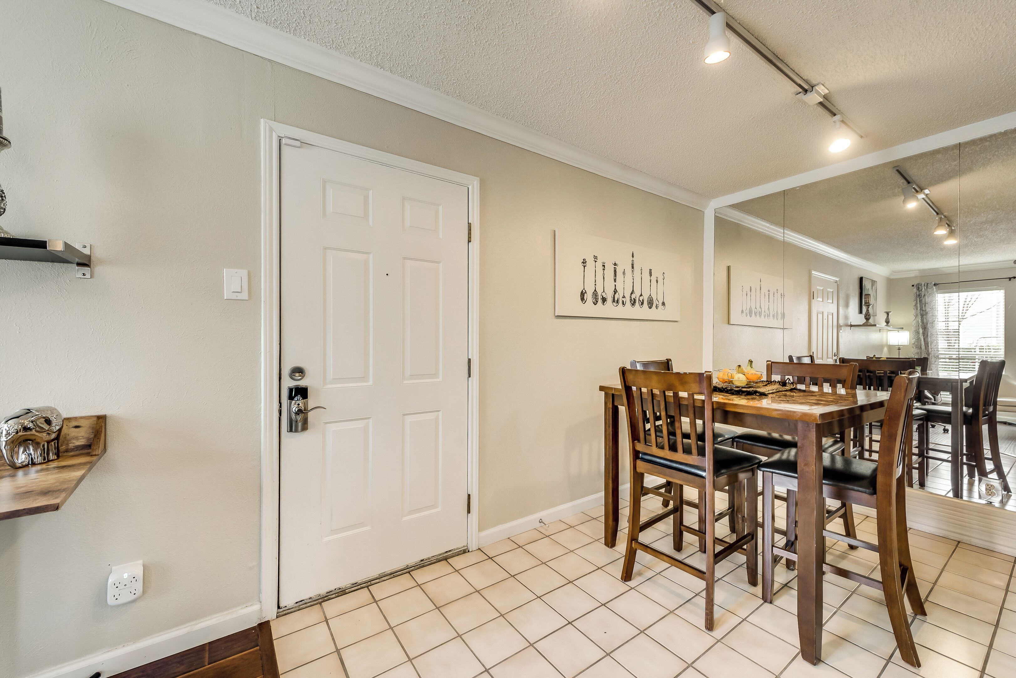 A dining area with a wooden table and chairs, a white door with a key lock, and a wall-mounted light fixture.