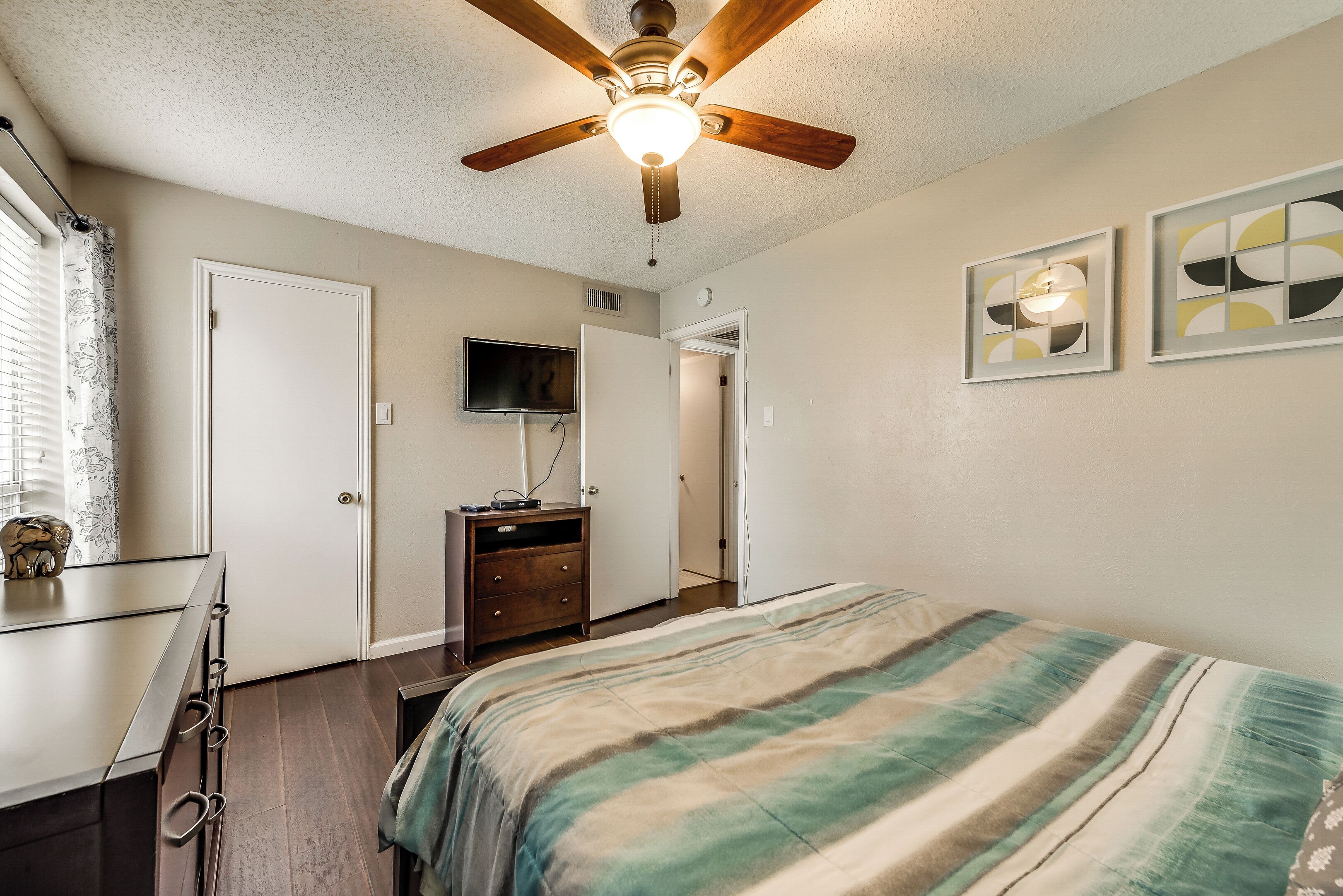 A bedroom with a bed, a ceiling fan, a TV, and a dresser.