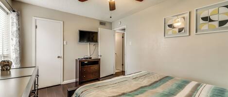 A bedroom with a bed, a ceiling fan, a TV, and a dresser.