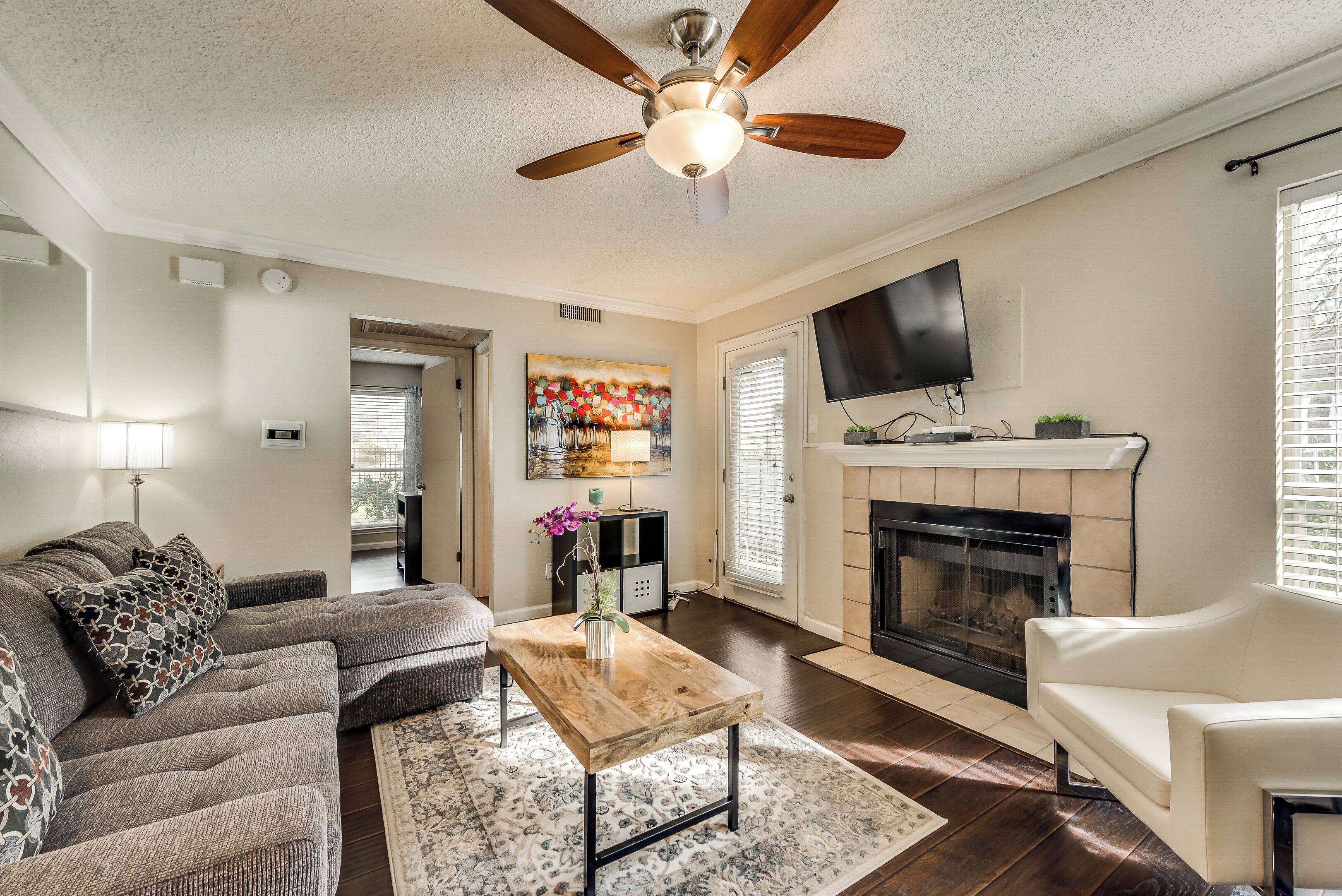A living room with a sofa, coffee table, fireplace, TV, and ceiling fan.