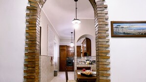 A kitchen with a tiled floor, wooden cabinets, a dining table with chairs, and a hanging light fixture. - Oasi d'Oltremare (Naples)