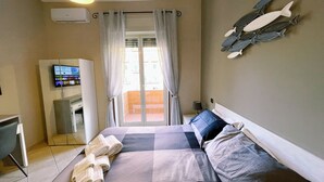 A hotel room with a bed, a TV on the wall, a balcony with curtains, and a mounted fish decoration. - Oasi d'Oltremare (Naples)