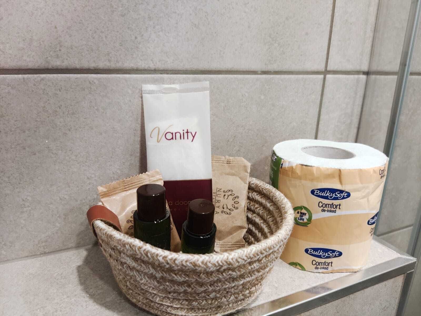 Un estante de baño con una bolsa de tocador, un rollo de papel higiénico y una cesta con artículos de aseo.