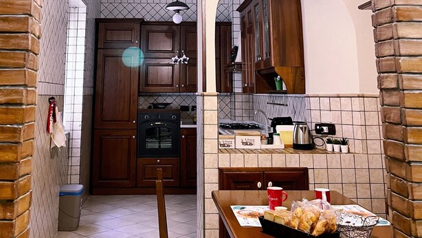 A kitchen with a brick archway, wooden cabinets, a dining table with a basket of bread, and a hanging light fixture. - Oasi d'Oltremare (Naples)