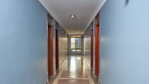 Ein langer, schmaler Korridor mit blauen Wänden und Holztüren, der zu einem hellen Raum mit einem großen Fenster führt.