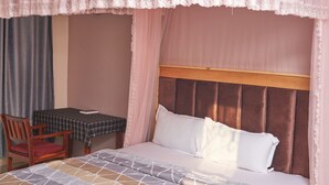 Ein ordentlich bezogenes Bett mit einem gemusterten Bettüberwurf, einem hölzernen Kopfteil und einem Tisch mit kariertem Tischläufer und einem Buch.