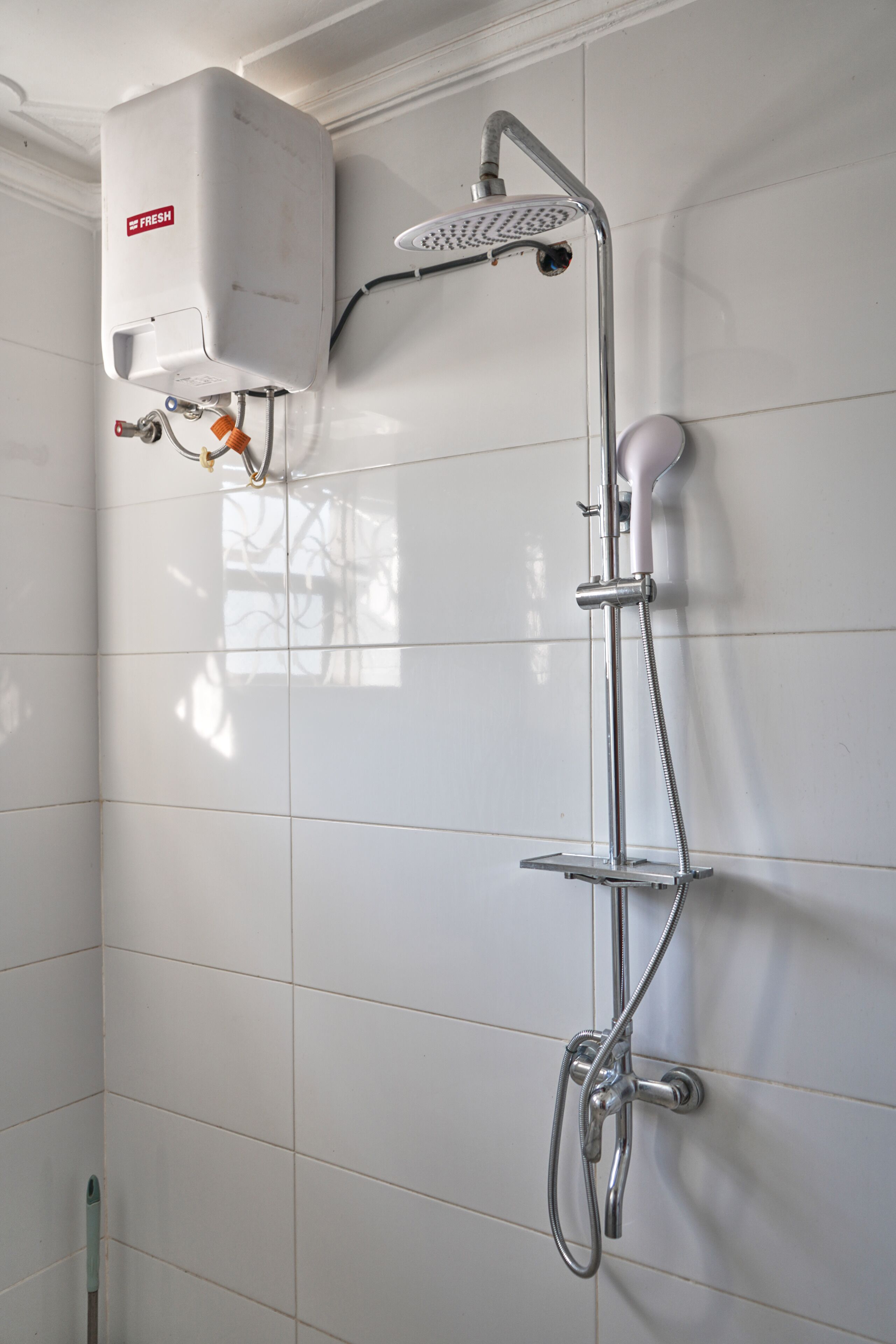 A bathroom with a wall-mounted shower, a water heater, and a hand showerhead.