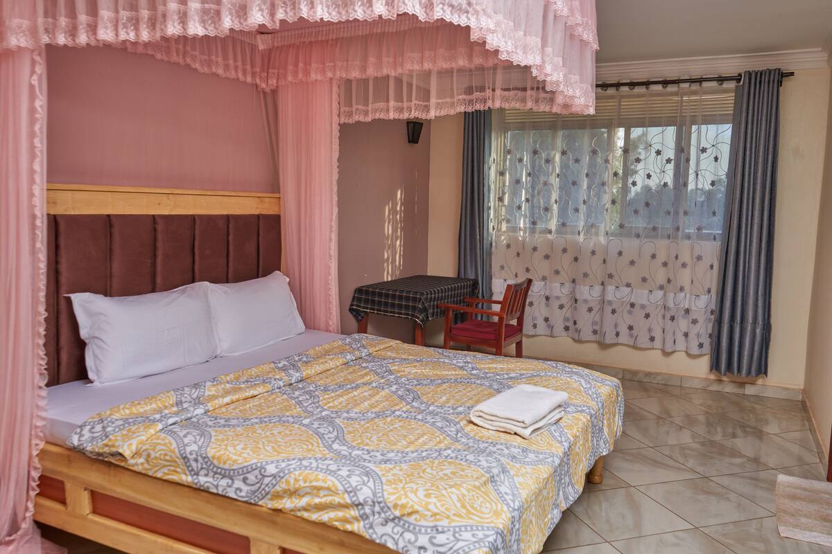 A bedroom with a bed, a table, a chair, and a window with curtains.