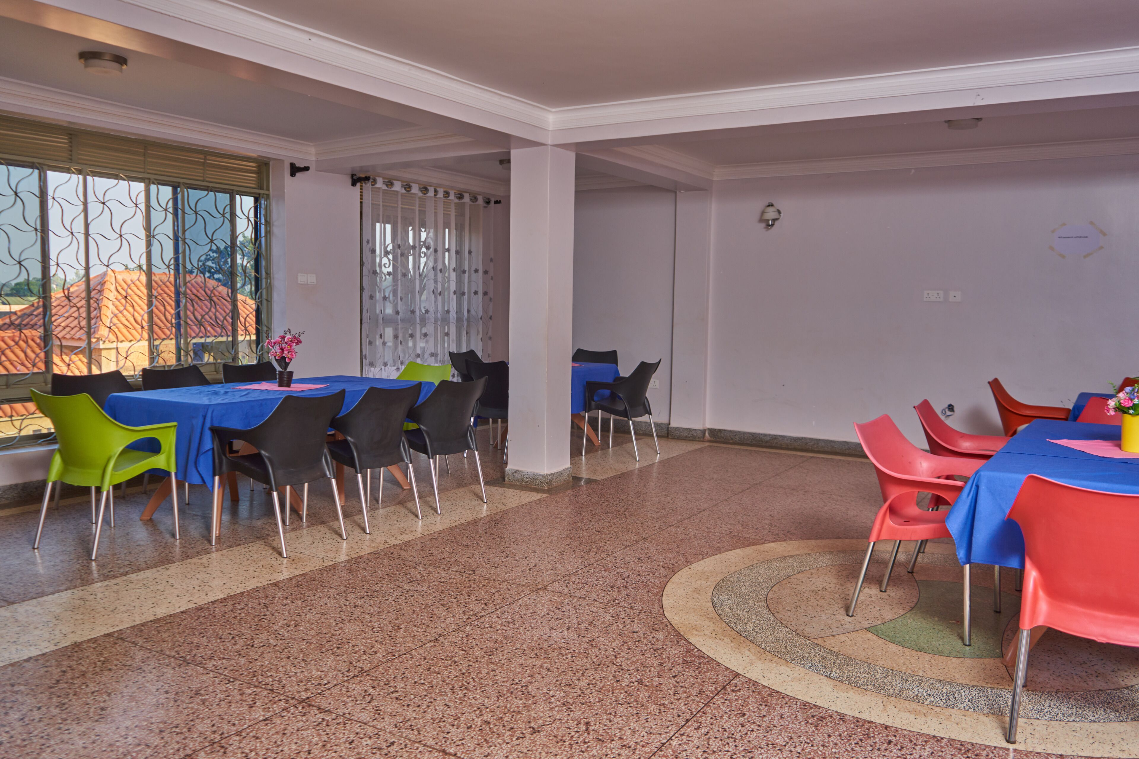 A dining area with tables and chairs, a patterned floor, and a window with blinds.
