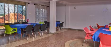 A dining area with tables and chairs, a patterned floor, and a window with blinds.