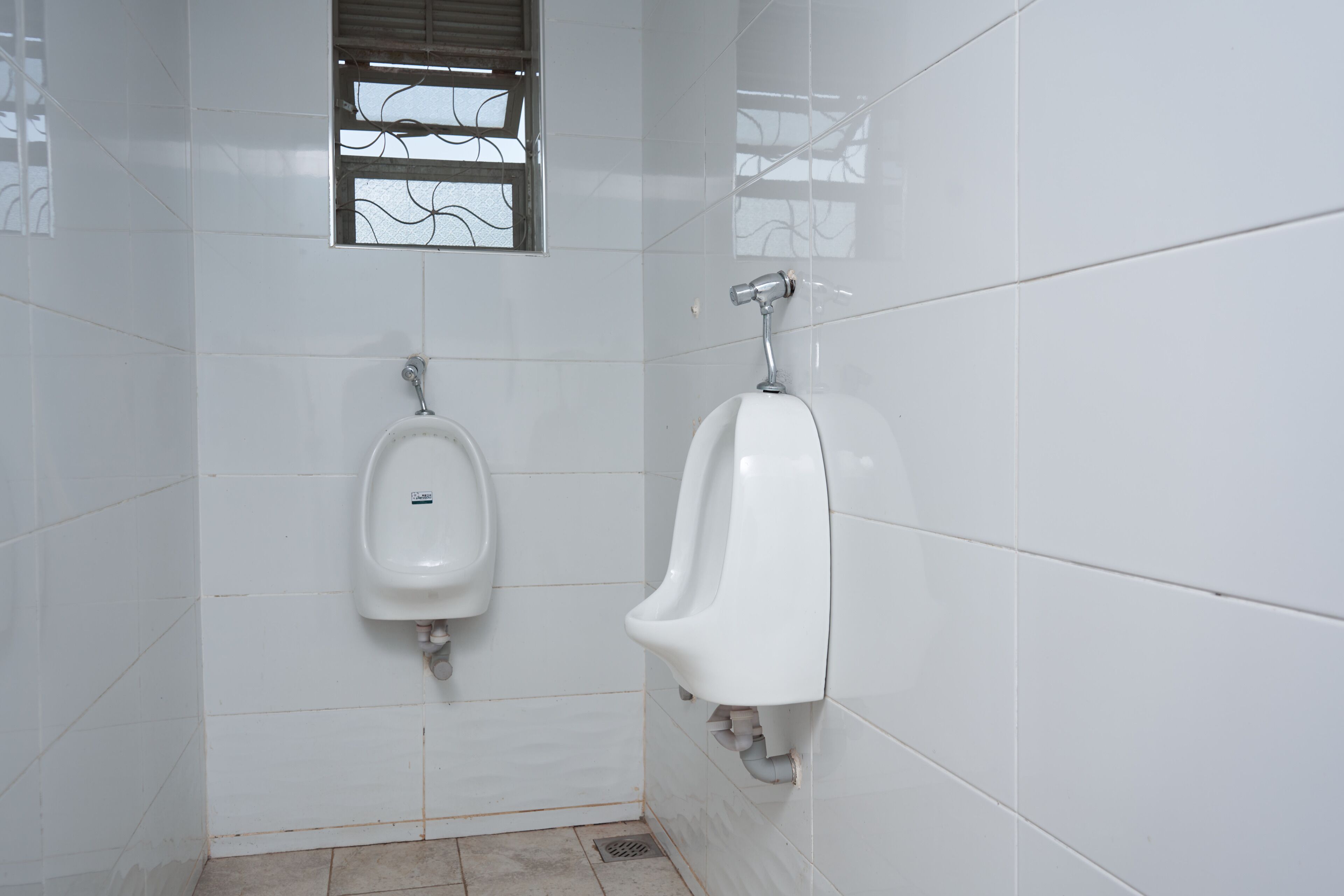 Een toiletruimte met witte betegelde wanden, een urinoir en een toilet.