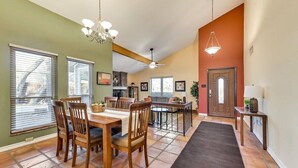 A spacious dining area with a wooden table and chairs, a kitchen in the background, and a hallway leading to a door. - Willow Bend: 4-Bedroom Tranquil Escape (Bedford)