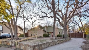 A two-story house with a front yard, a stone retaining wall, and a wooden staircase leading to the front door. - Willow Bend: 4-Bedroom Tranquil Escape (Bedford)