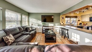A modern living room with a sofa, a coffee table, and a kitchen area with a bar and stools. - Willow Bend: 4-Bedroom Tranquil Escape (Bedford)