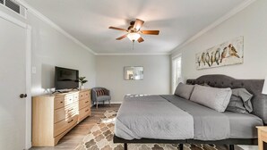 A bedroom with a bed, a dresser, a television, a ceiling fan, and a painting on the wall. - Willow Bend: 4-Bedroom Tranquil Escape (Bedford)