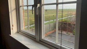 A window with white frames and a view of a grassy field and a fence. - Nollaig  Beachside Bliss - Pass the Keys (Rye)