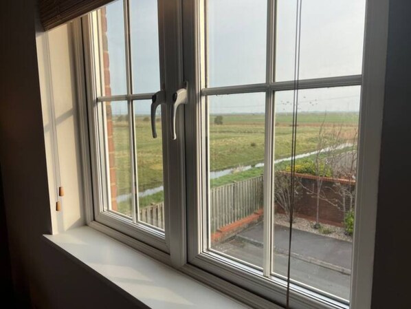 A window with white frames and a view of a grassy field and a fence.