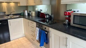 A modern kitchen with white cabinets, a black countertop, a stove, a microwave, and a coffee machine. - Nollaig  Beachside Bliss - Pass the Keys (Rye)