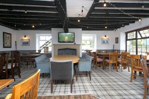 A cozy dining area with a fireplace, wooden furniture, and a television mounted above the fireplace.