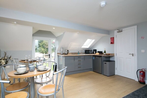 A modern kitchen with a dining area, featuring a skylight, grey cabinets, and a small dishwasher.