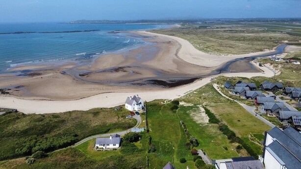 An aerial view of a coastal area with a sandy beach, a white house with a driveway, and a cluster of houses with sloped roofs. - Self Contained Apartment at Country Pub Restaurant - Pass the Keys (Llanddona)