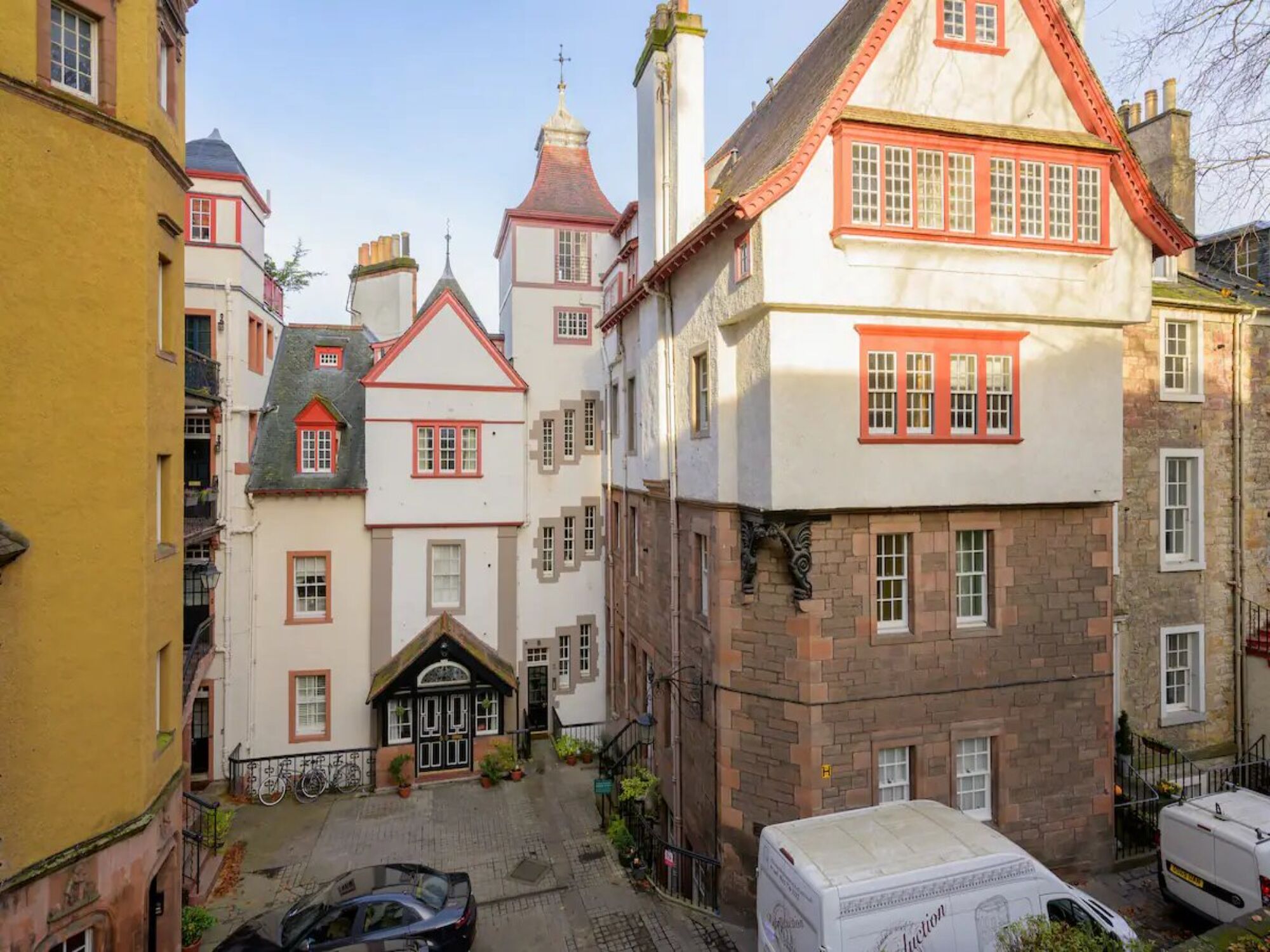Uma rua estreita com edifícios históricos, incluindo uma casa notável com telhado de telhas vermelhas e fachada branca.