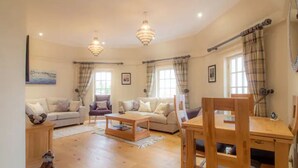 A spacious living room with a wooden floor, a sofa set, a dining table with chairs, and two pendant lights.