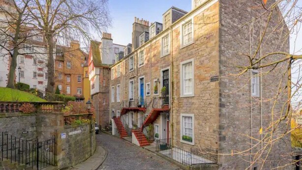 A narrow cobblestone street flanked by historic stone buildings with multiple stories, some featuring external staircases.