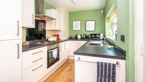 A compact kitchen with white cabinets, a black countertop, and a green wall. There are two framed pictures on the wall, a microwave, and a kettle.