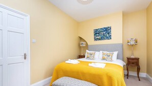 A bedroom with a bed, bench, bedside tables, and a painting on the wall.