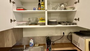 A kitchen with open cabinets displaying various kitchenware, a sink, and a microwave. - Studio apartment  in Verdun, "Les Coulisses" (Verdun)