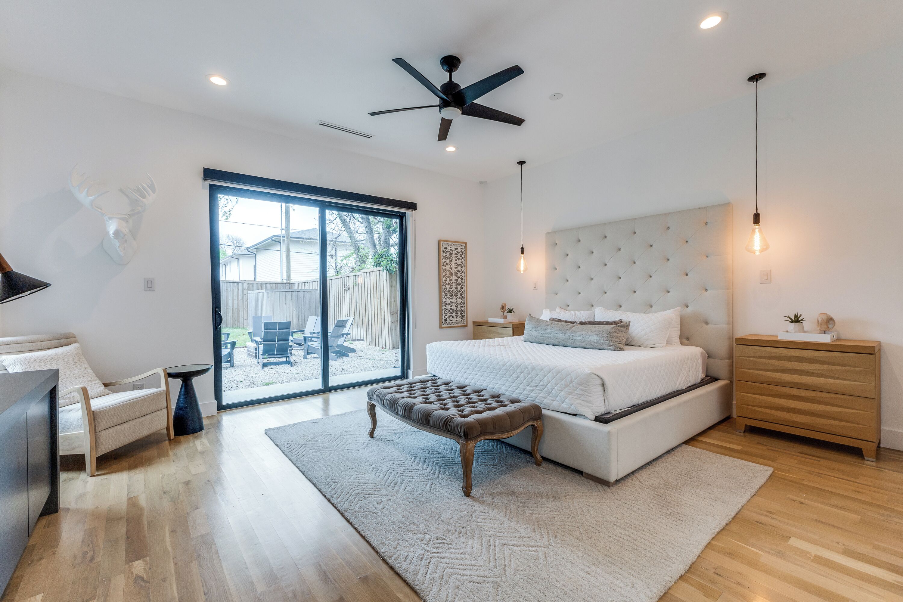 A modern bedroom with a large bed, a ceiling fan, a sliding glass door, and a view of the outdoors.