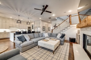 A spacious living room with a large grey sectional sofa, a fireplace, and a staircase with wooden railings.