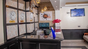 A reception area with clocks labeled 'Paris' and 'Nakurumi', a digital screen, and a wall-mounted TV. - WAFFLES SUITES (Nakuru)