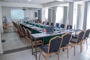 Un salón de conferencias con una larga mesa, sillas, computadoras portátiles y una pantalla para proyector.