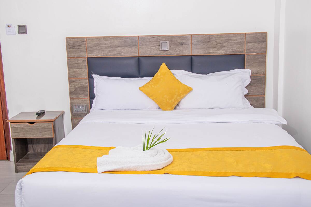 Una cama bien hecha con una colcha blanca y amarilla, una sola almohada amarilla y una toalla blanca en el reposapiés.