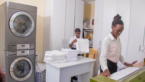 A laundry area with a washing machine, a table with folded towels, and a green cabinet. - WAFFLES SUITES (Nakuru)