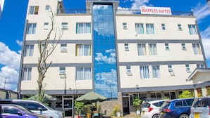 A multi-story hotel with a sign reading "The Waffles Suites" and a large glass window reflecting the sky. - WAFFLES SUITES (Nakuru)